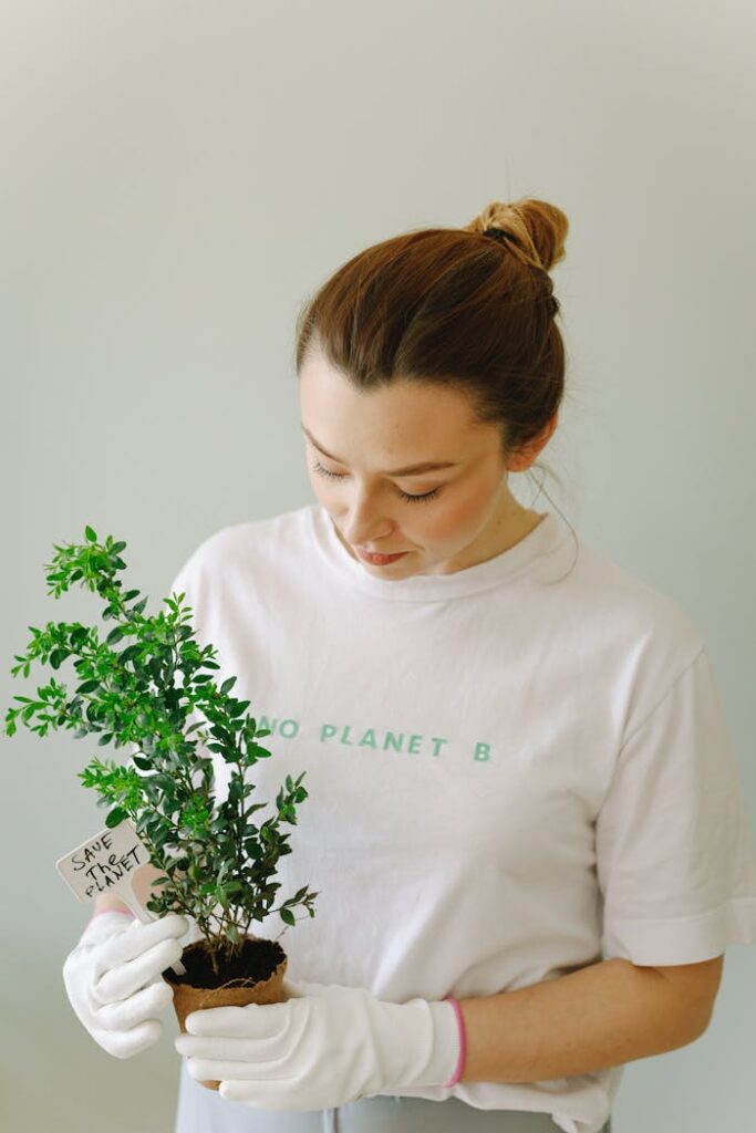 pexels-photo-7655918 Woman in white shirt holds a potted plant with 'save the planet' tag, promoting eco-awareness.