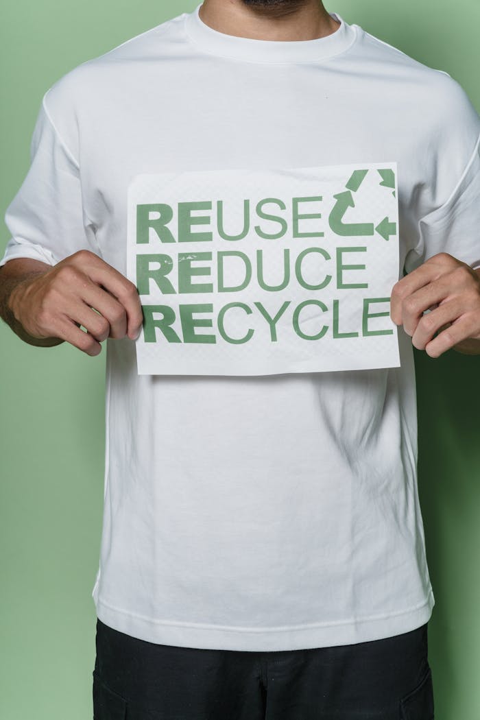 A man in a white shirt holding a sign promoting recycling with the words 'reuse, reduce, recycle'.